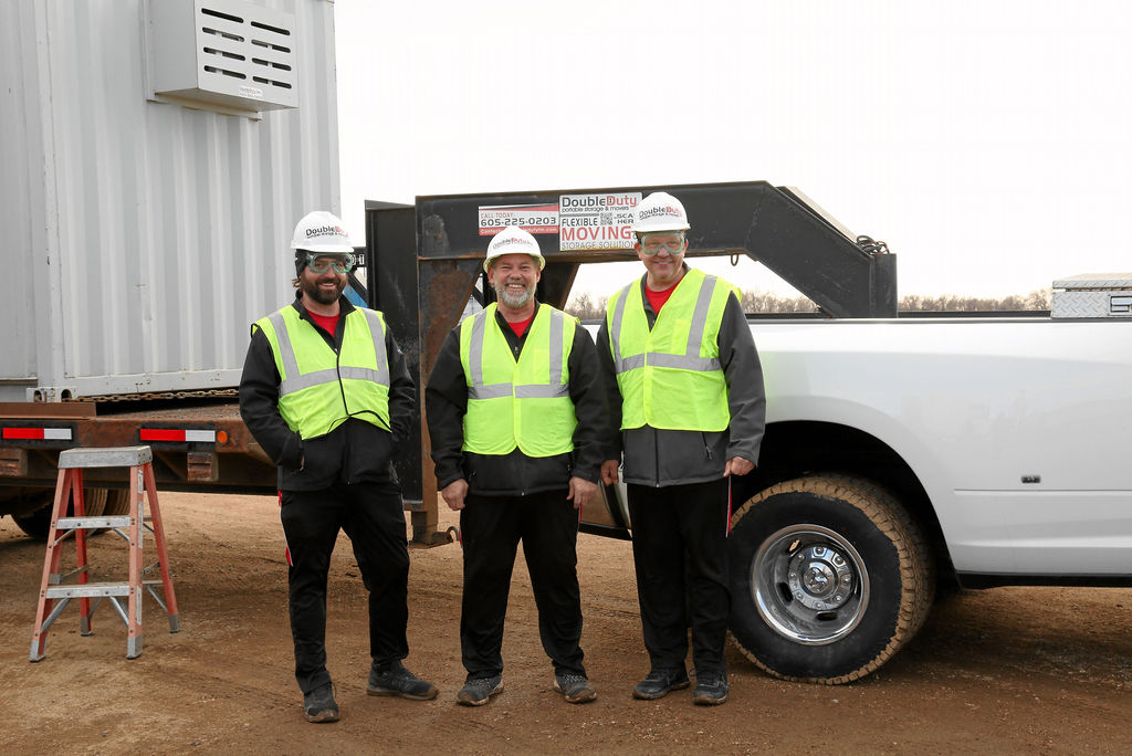 Three men in safety vests standing next to a truck.