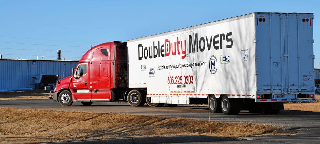 A red truck driving down the road with a white trailer.