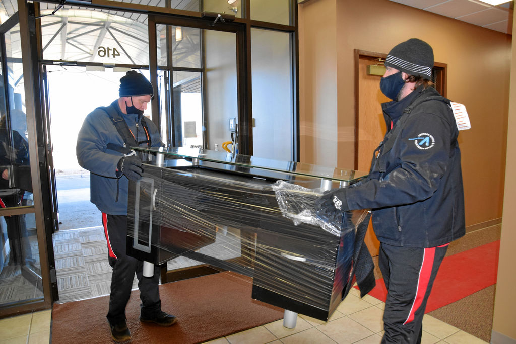 Two men in black jackets and masks unloading a piano.