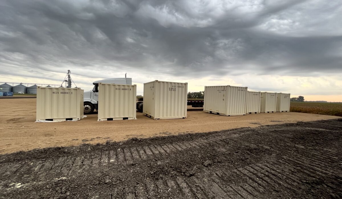 A group of white containers sitting on top of a dirt field.